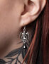 Close-up of a person wearing silver dropper earrings with a circular design and a black gemstone.