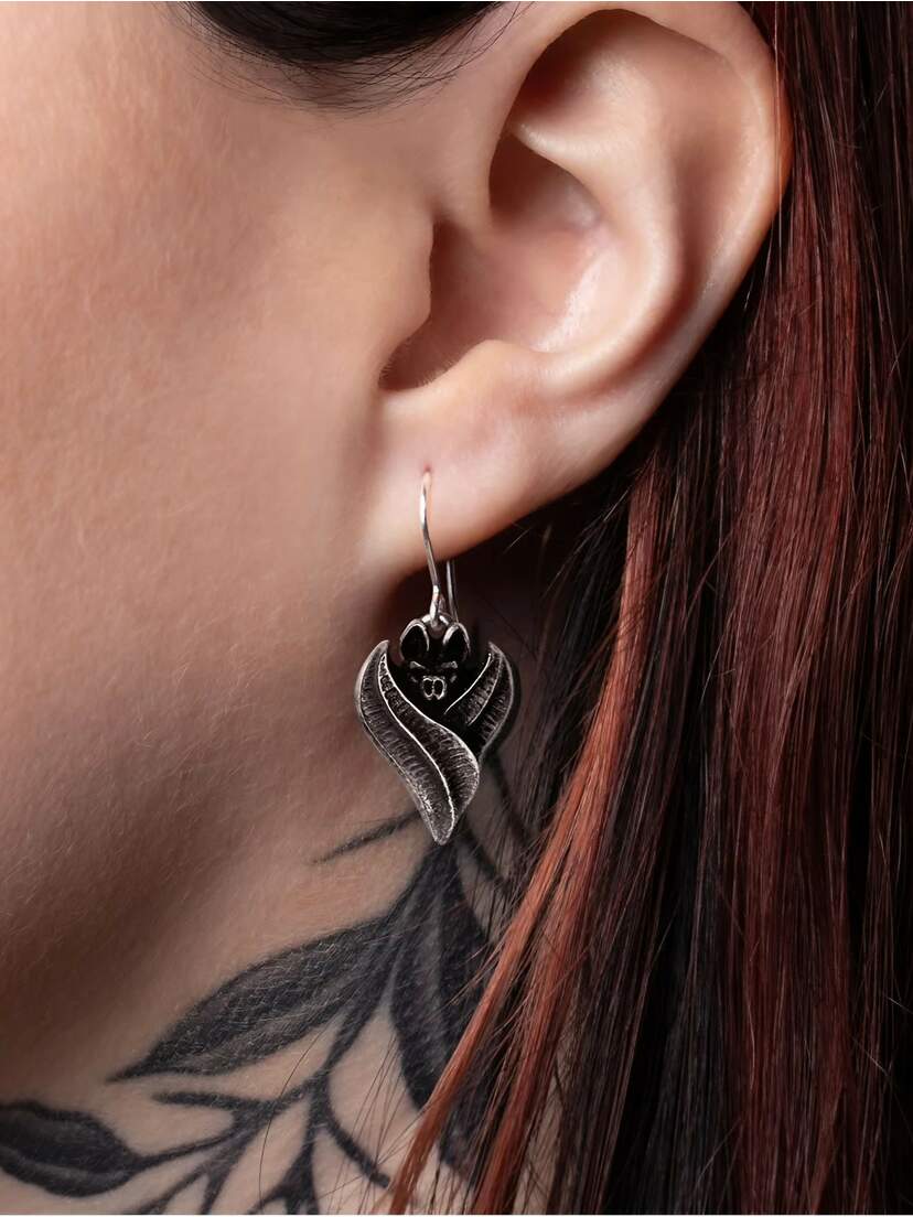 Close-up of a person's ear wearing Gothic bat dropper earrings with intricate design.