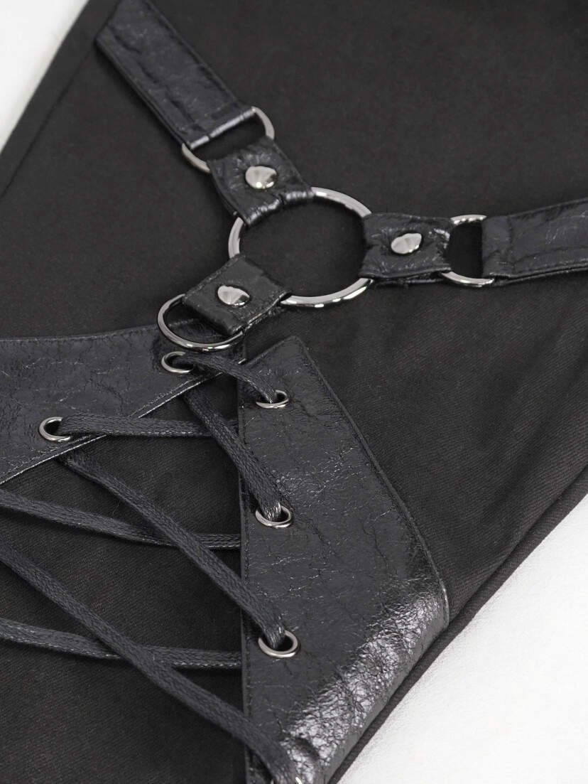 Close-up of black harness pants featuring straps and metal rings for a stylish design.